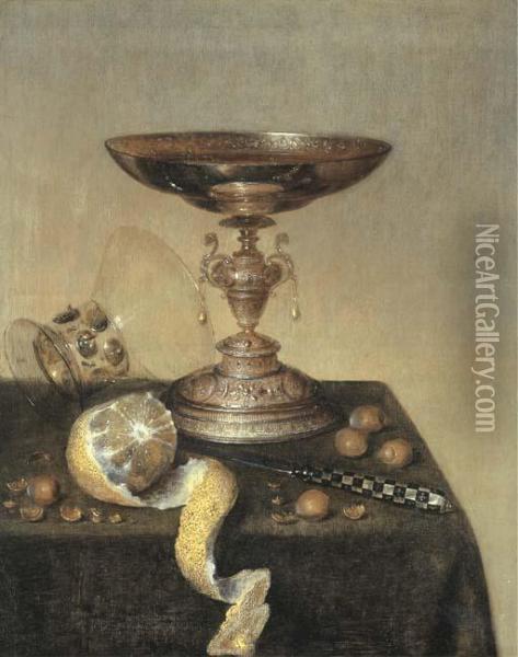 A Silver Tazza, An Upturned Roemer, A Partly-peeled Lemon, A Knifeand Hazelnuts On A Draped Table Oil Painting - Maerten Boelema De Stomme